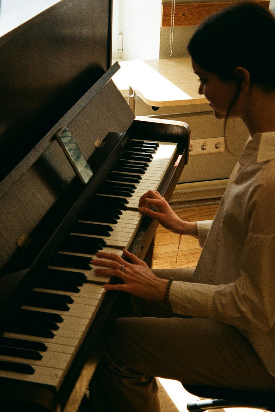 Giovane donna suona il pianoforte con uno smartphone sul leggio.
